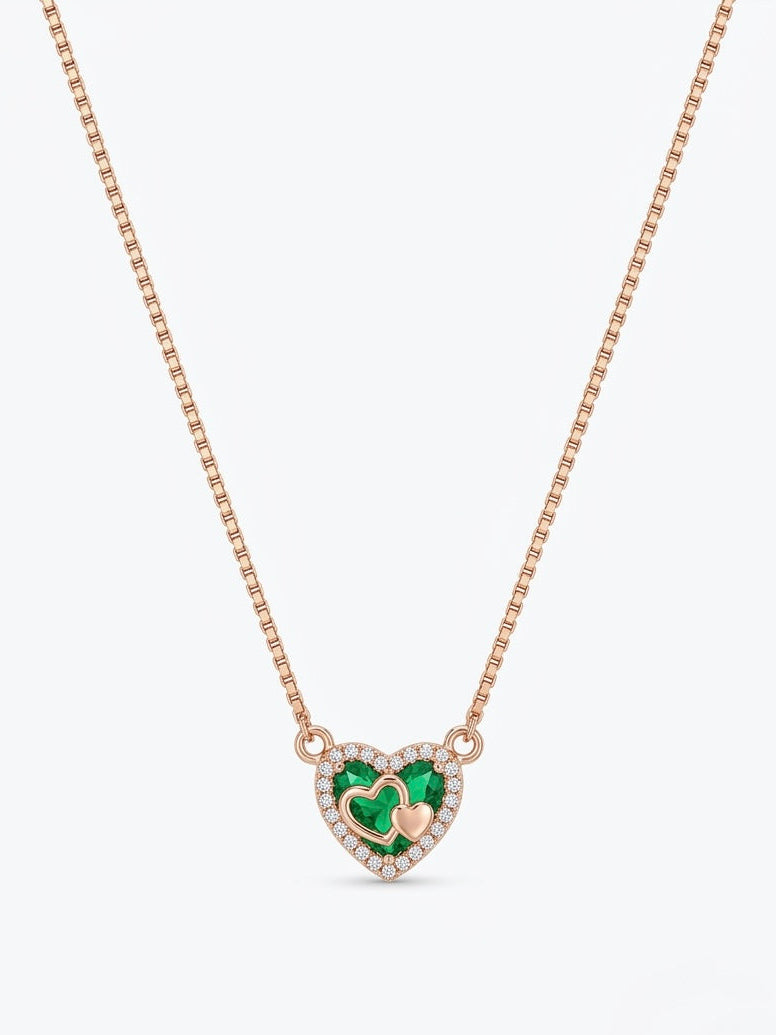 A rose gold box chain necklace featuring a heart-shaped pendant with a green heart in the center, surrounded by a halo of small clear stones and a tiny gold heart.